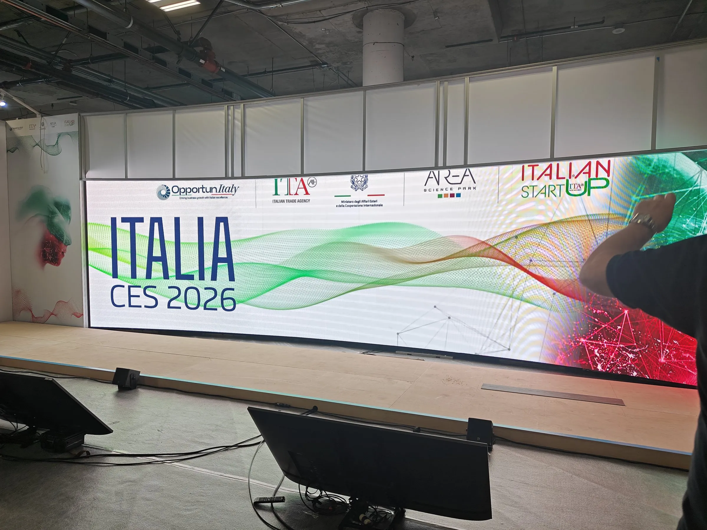 A curved LED wall reading Italia CES 2026 built along the back of a trade show stand, with monitors on stands in front of it.